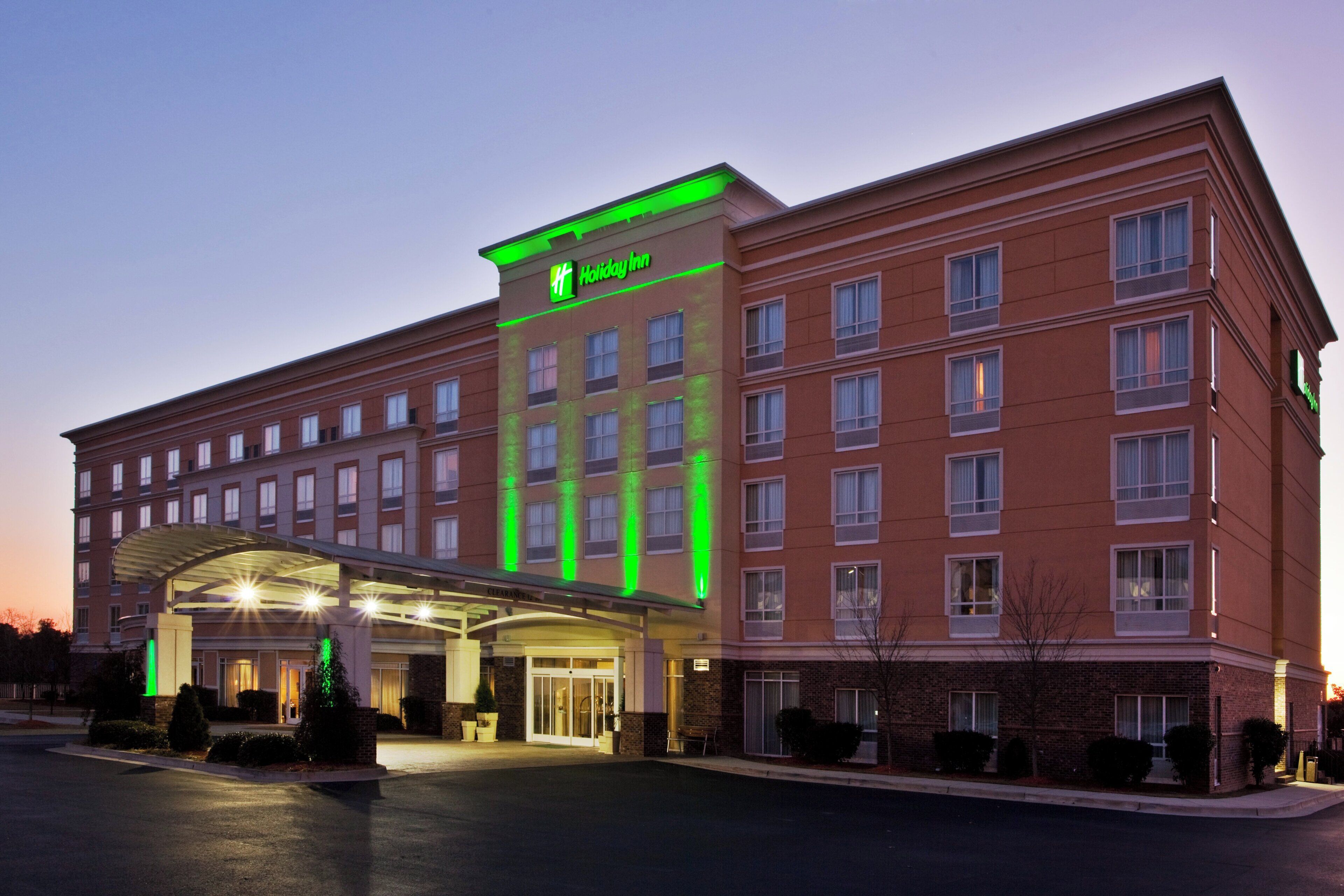 Ein mehrstöckiges Holiday Inn Hotel mit auffälligem grünen Schild, überdachter Eingangsbereich und Parkplatz.