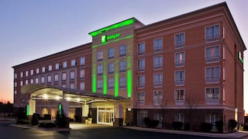 Ein mehrstöckiges Holiday Inn Hotel mit auffälligem grünen Schild, überdachter Eingangsbereich und Parkplatz.