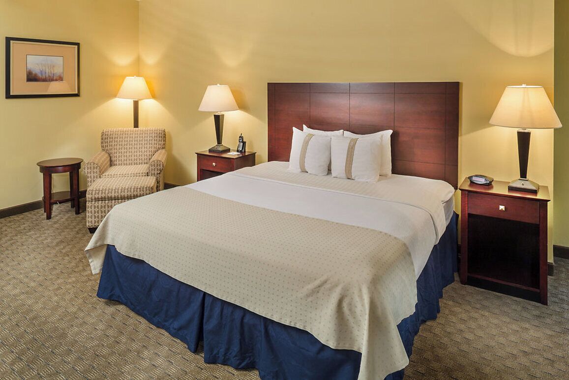 A hotel room with a large bed, two bedside tables with lamps, a chair, and a small table.