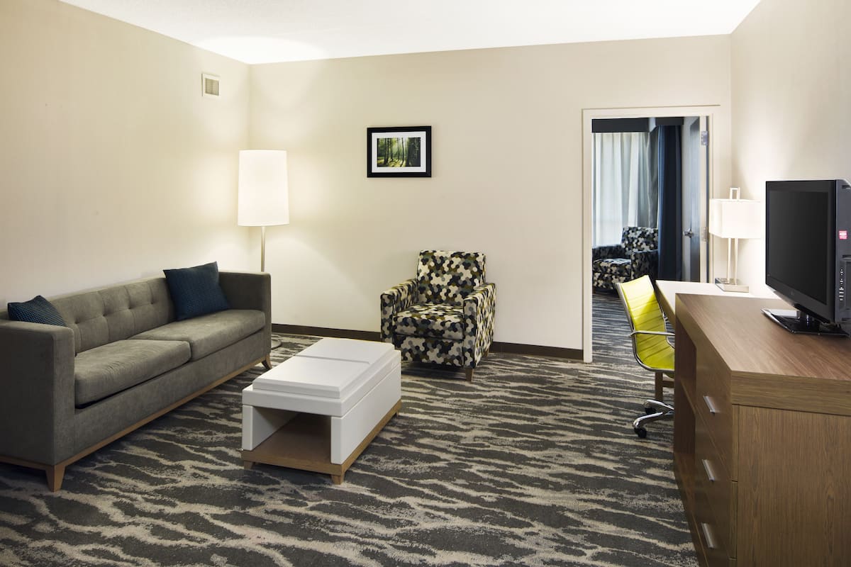 A hotel room with a sofa, armchair, TV, and a desk.
