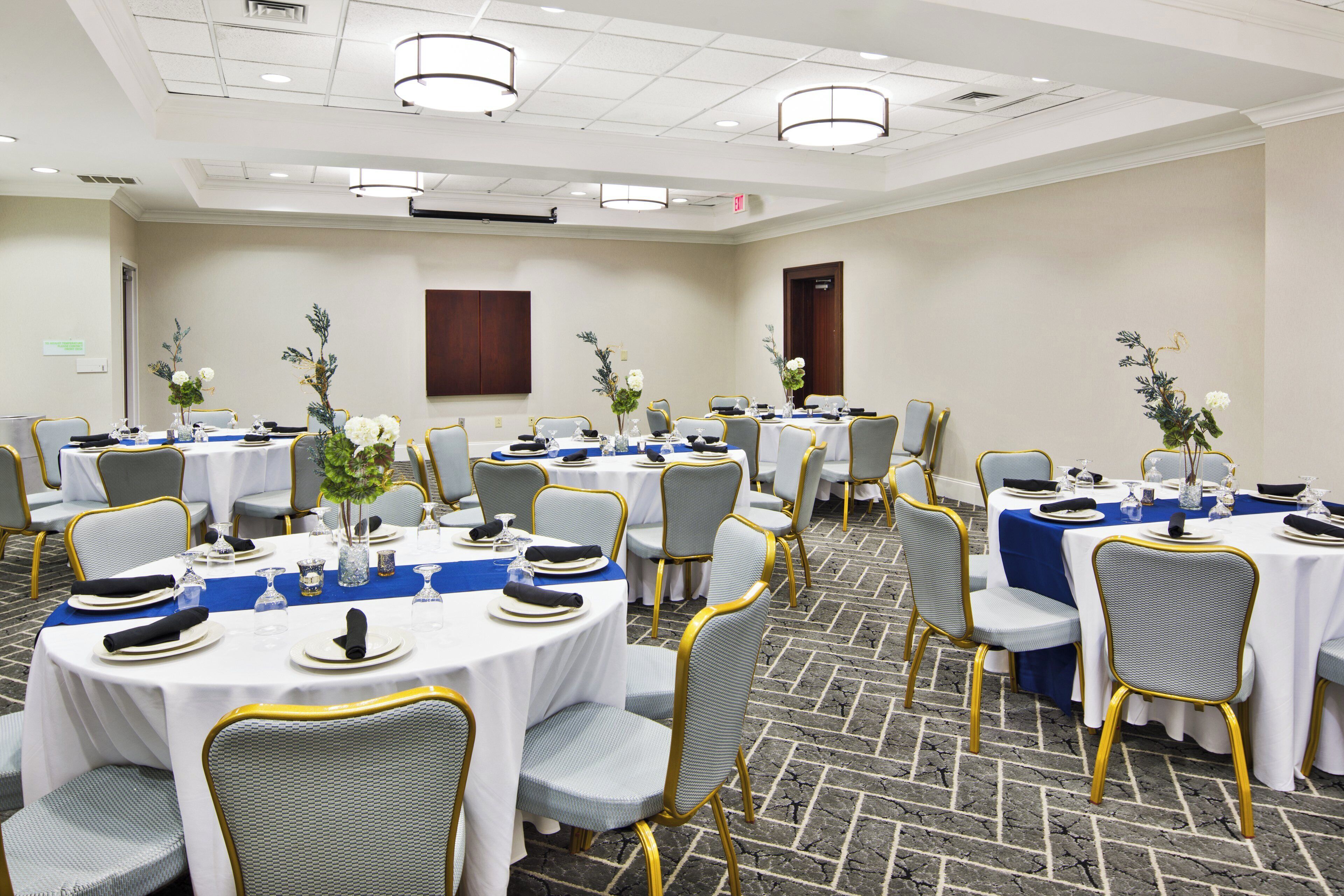 A conference room with round tables, grey chairs with gold accents, and white tablecloths.