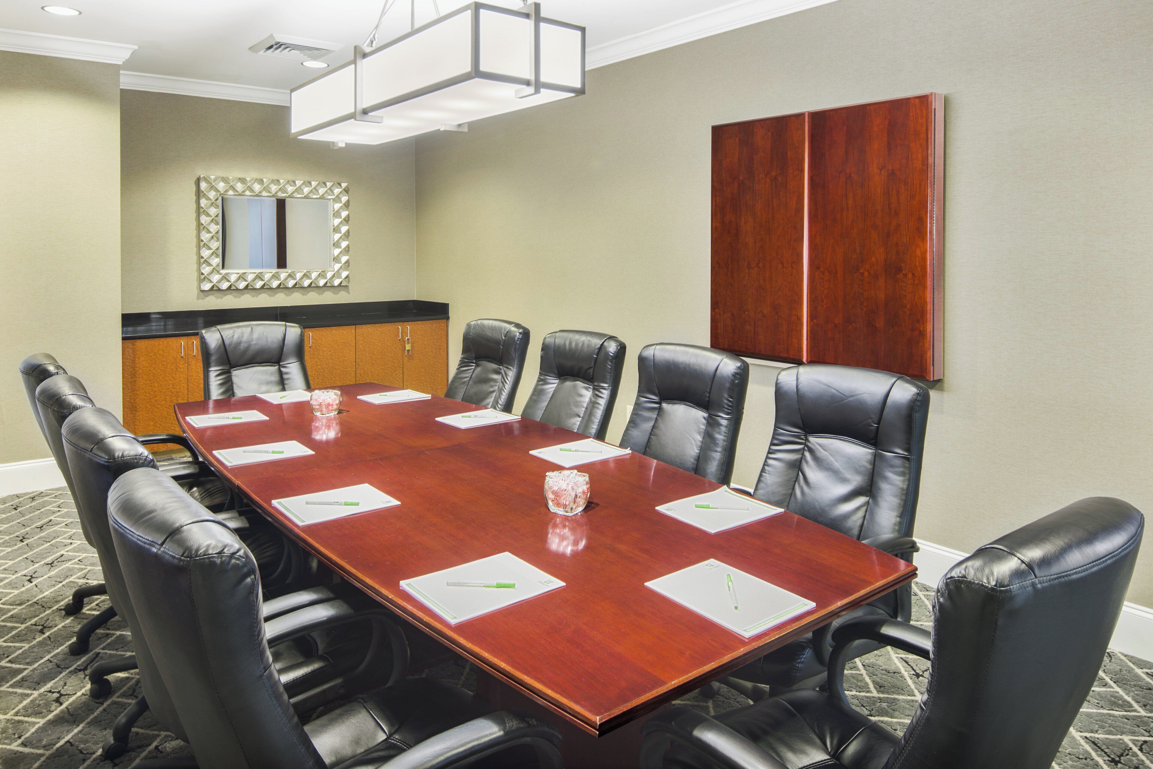 A conference room with a rectangular table, six leather chairs, a mirror, and a wooden panel on the wall.
