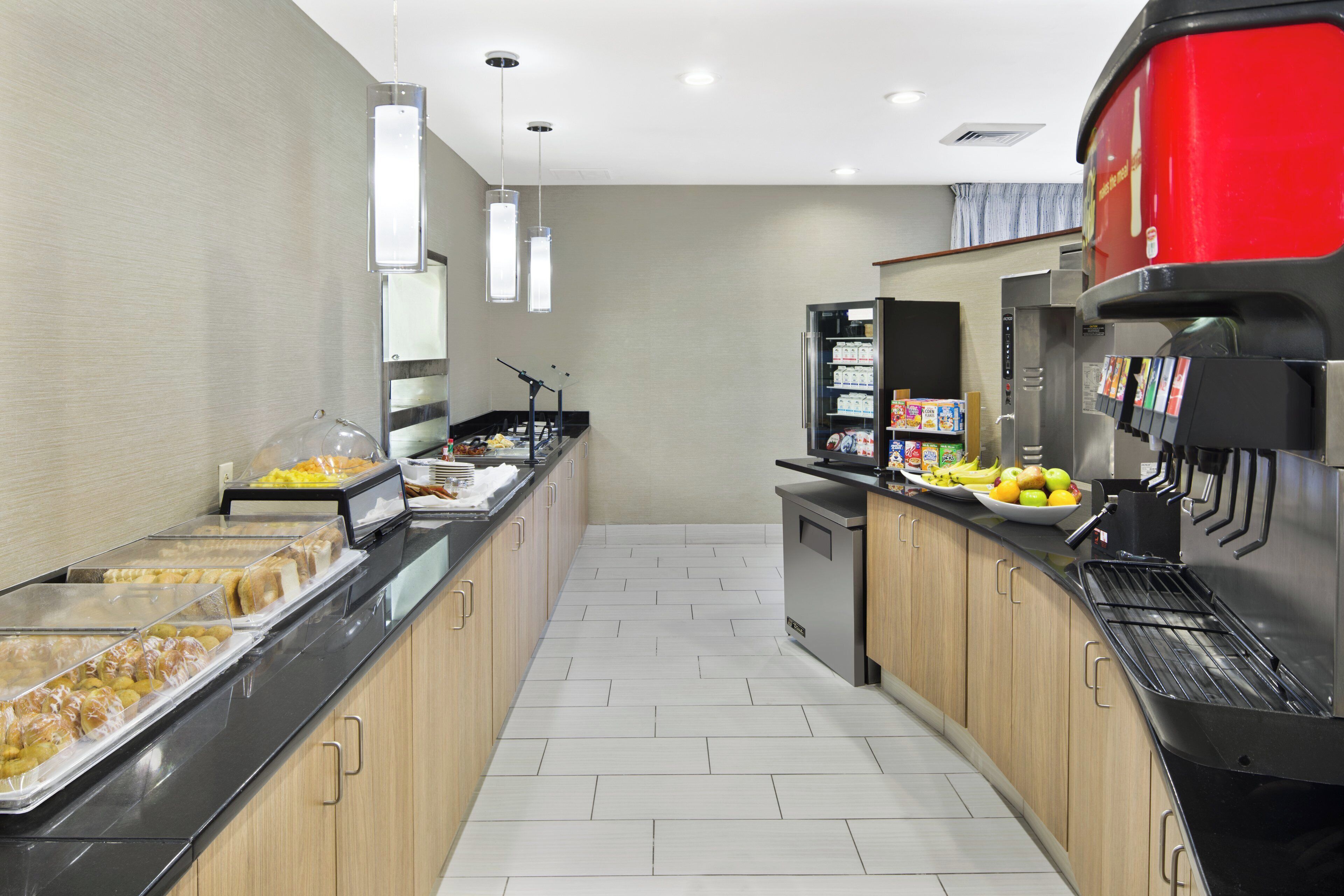 Een ontbijtruimte met self-service faciliteiten, diverse etenswaren, een koffieapparaat en een koelkast vol drankjes.