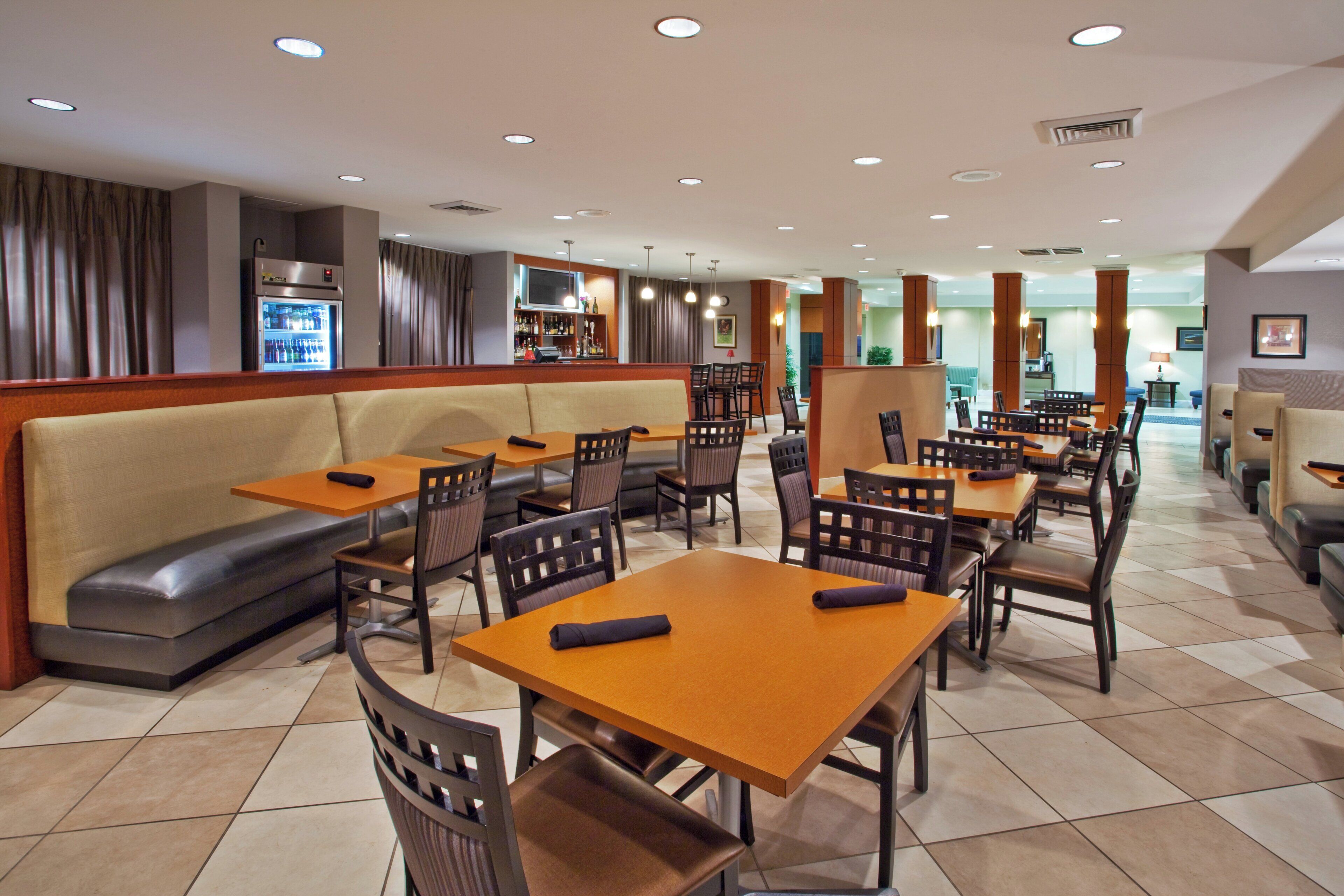 A restaurant with booths, tables, and chairs. There is a bar area with a TV and shelves of bottles.