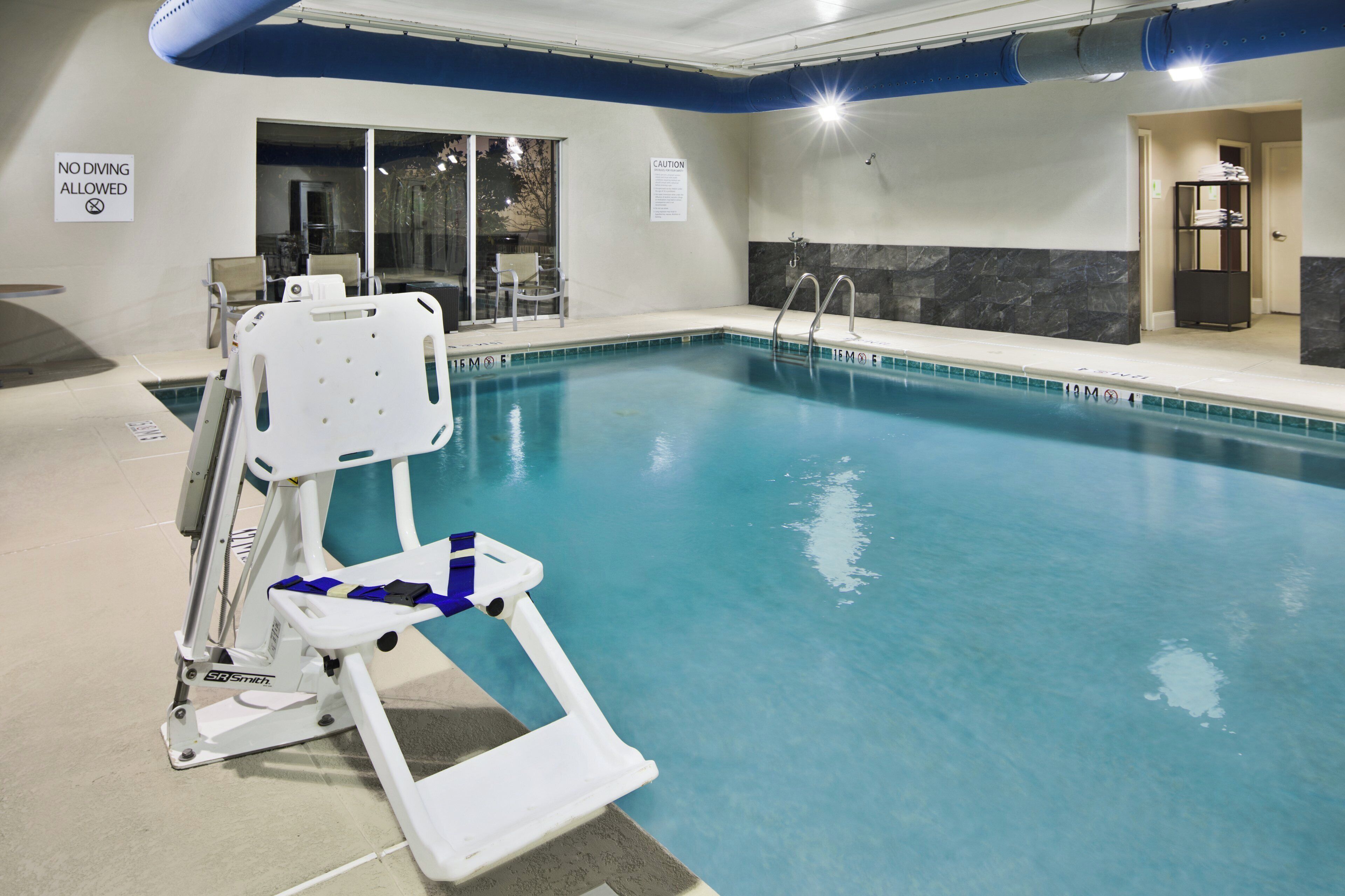 Ein Hallenbad mit Poollift, einem Sprungverbotsschild und einem Warnhinweis an der Wand.