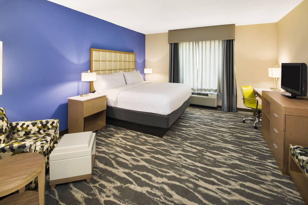 A hotel room with a bed, bedside tables, a desk with a chair, a television, and a window with curtains.