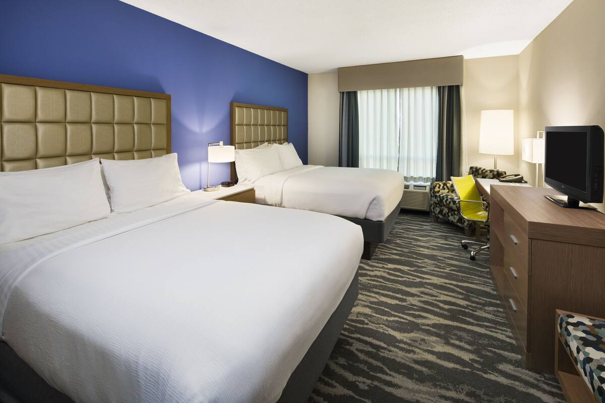 A hotel room with two beds, a desk with a television, a chair, and a desk lamp.
