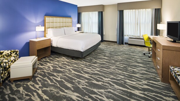 A hotel room with a large bed, a desk with a computer, a chair, a TV, and a window with curtains. - Holiday Inn Augusta West I-20 by IHG (Grovetown)