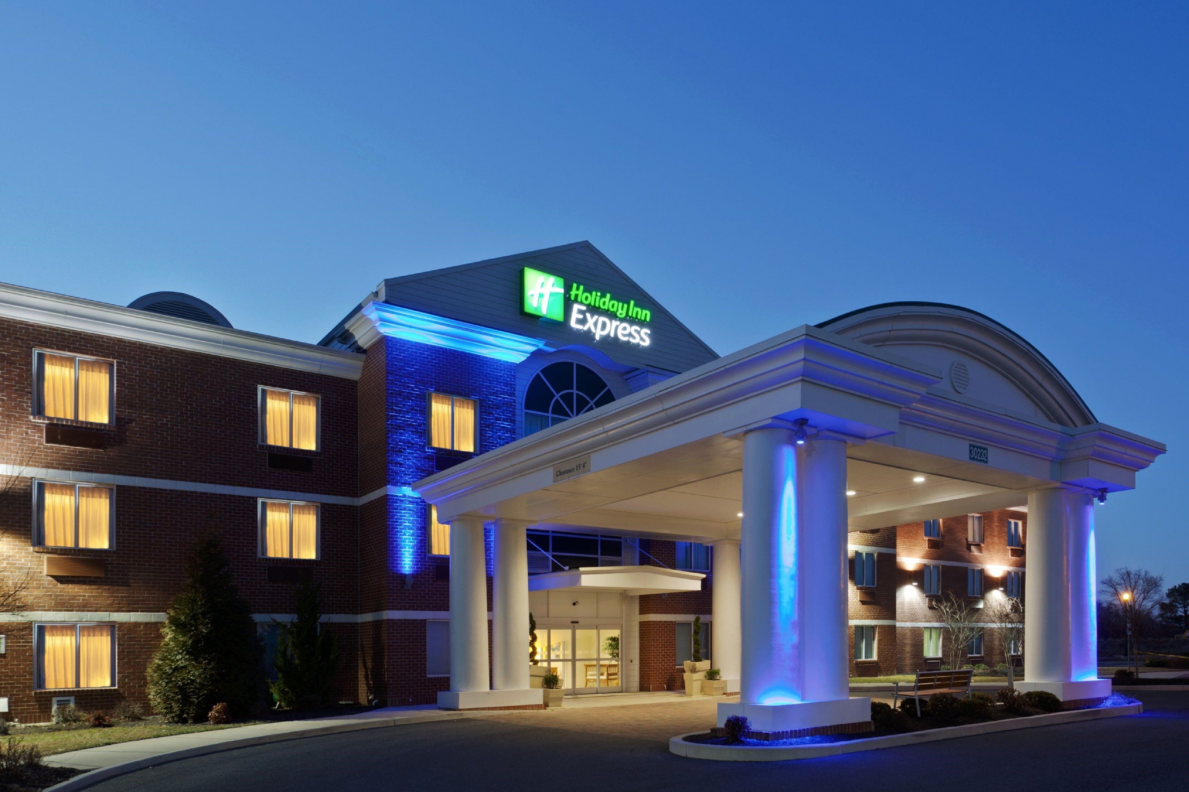 Un hotel Holiday Inn Express con fachada de ladrillo, una entrada cubierta y cielo despejado.