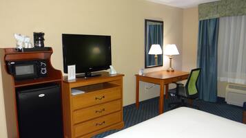 Ein Hotelzimmer mit Bett, Schreibtisch, Fernseher, Mikrowelle, Kühlschrank, Lampe und Stuhl.
