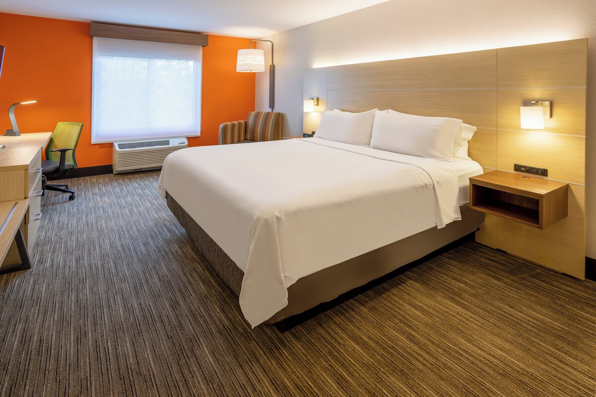 A hotel room with a large bed, a desk, a chair, and a nightstand.