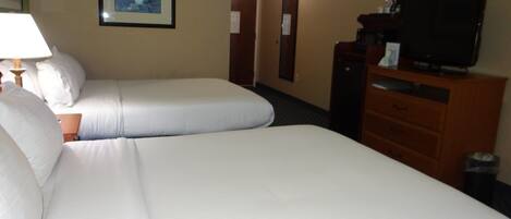 A hotel room with two beds, a television, a dresser, and a framed picture on the wall.