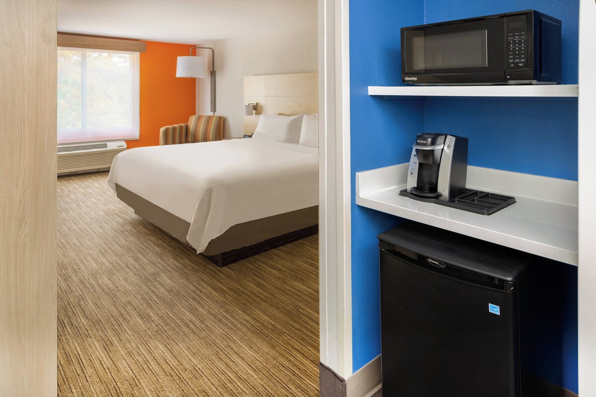 A hotel room with a bed, a coffee maker, a microwave, and a mini refrigerator.