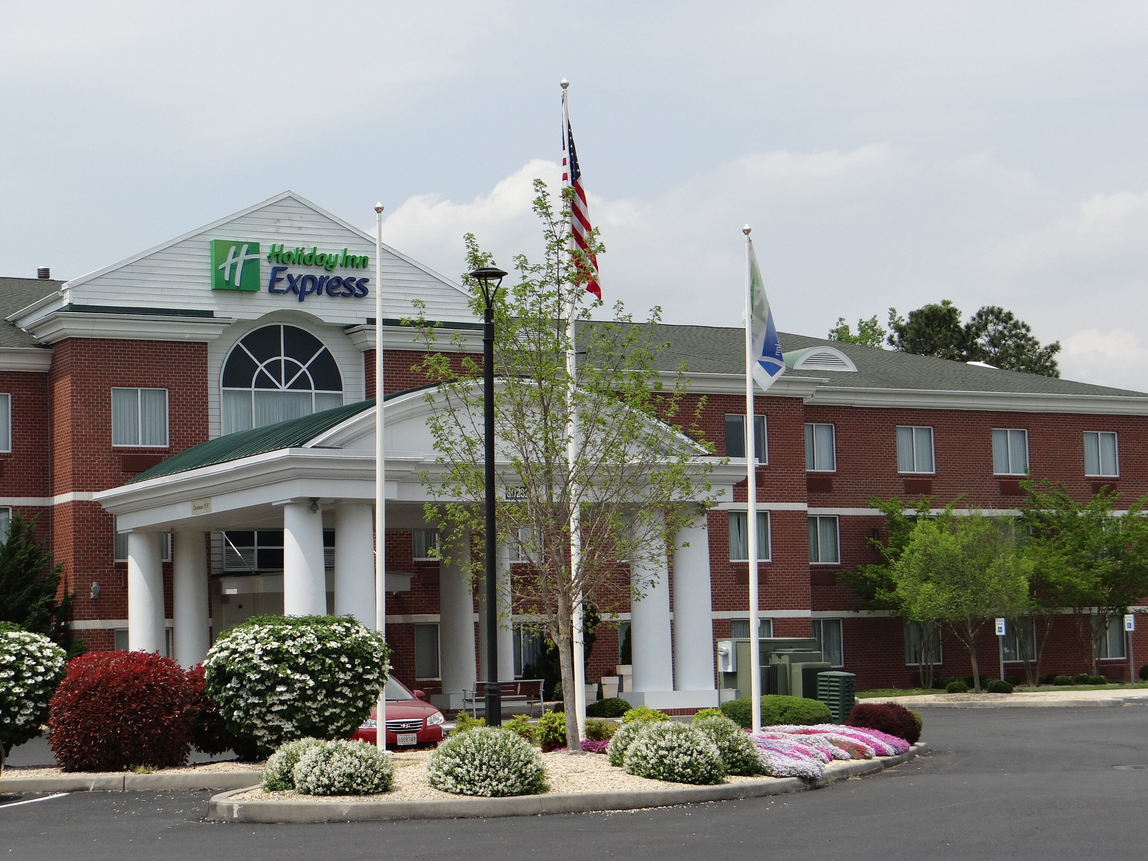 Un hotel Holiday Inn Express con facciata in mattoni, ingresso coperto e un'asta con la bandiera americana.