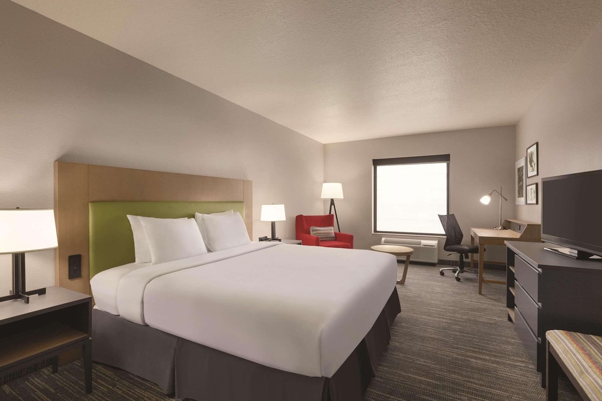 A hotel room with a large bed, a desk, a chair, a TV, and a window.