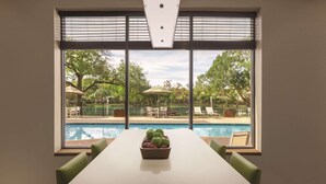 Un coin repas avec vue sur la piscine, une table sur laquelle se trouve un saladier rempli de fruits et des chaises vertes.