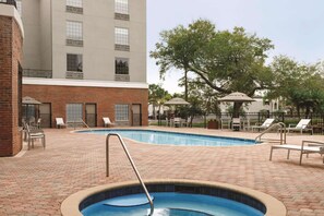 A swimming pool with a brick patio, lounge chairs, and a building with a brick facade and large windows.