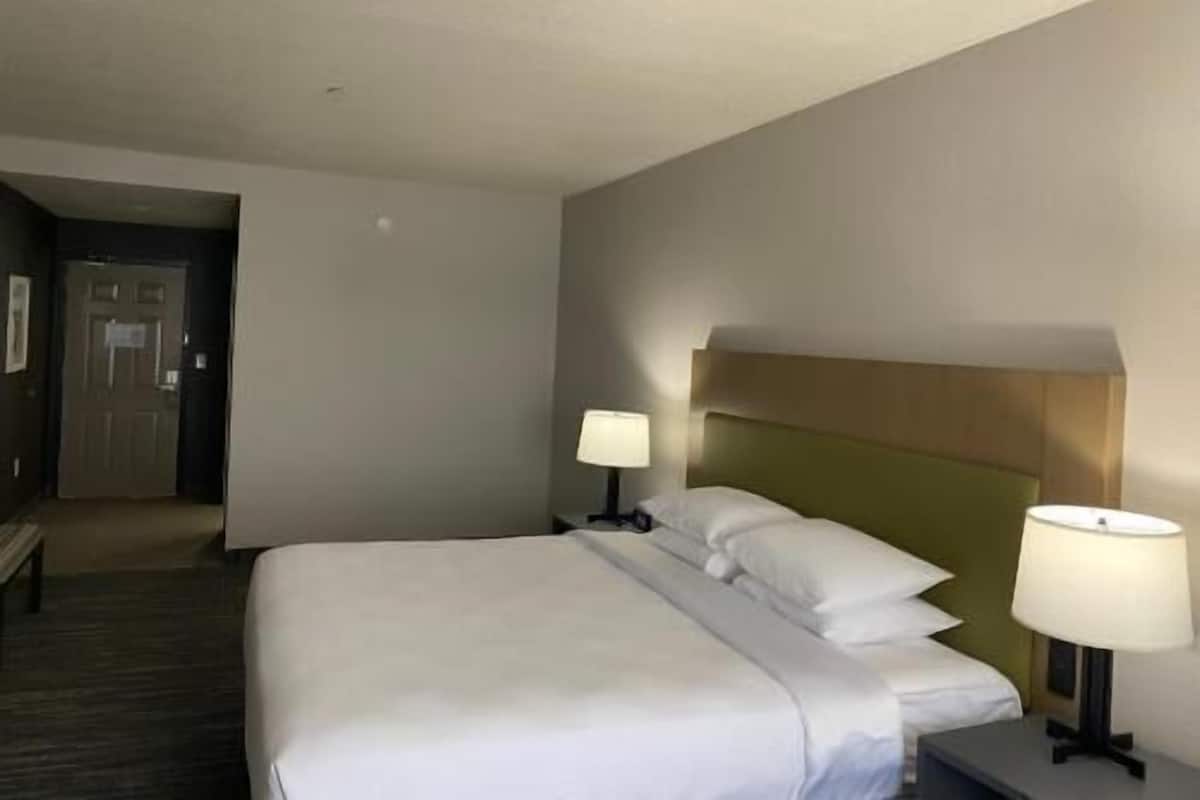 A hotel room with a large bed, two bedside tables with lamps, a wooden headboard, and a door leading to another room.