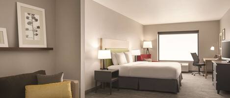 A hotel room with a bed, a desk, a chair, a sofa, and a small table.