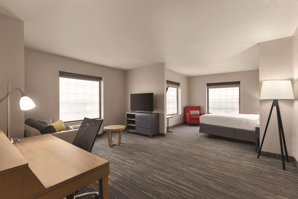 A hotel room with a bed, a desk, a TV, a sofa, and a lamp.