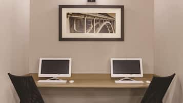 A room with two desks, each with a computer and keyboard, and a framed picture of a bridge on the wall.