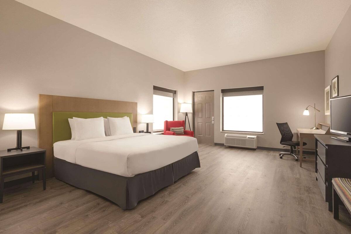 A hotel room with a large bed, a desk, a chair, a TV, and a window.
