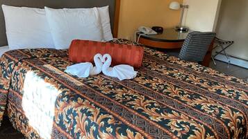 A hotel room with a large bed, a bedside table with a lamp, a chair, and a small round table with a phone.
