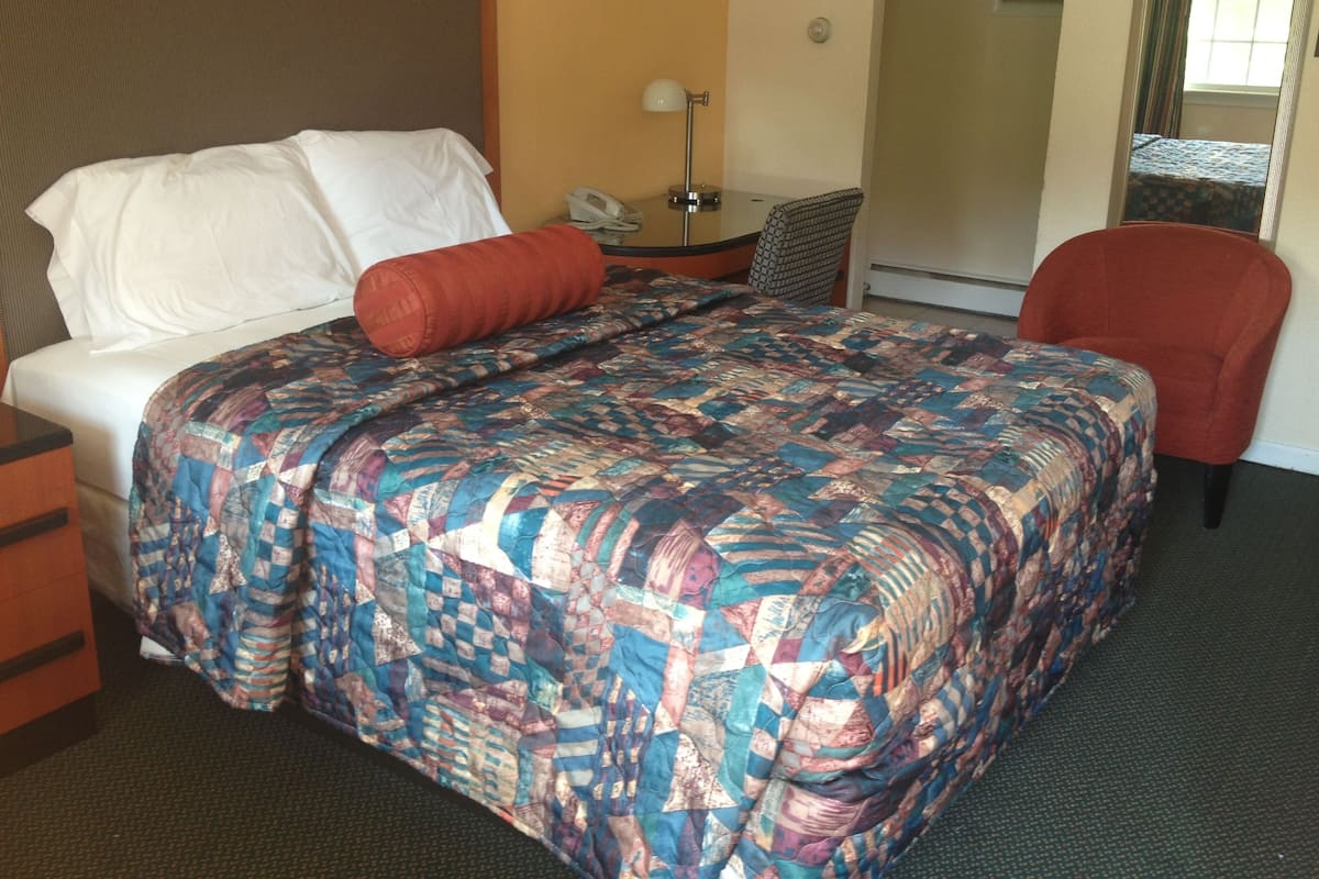 A hotel room with a bed, a desk, a chair, and a telephone.