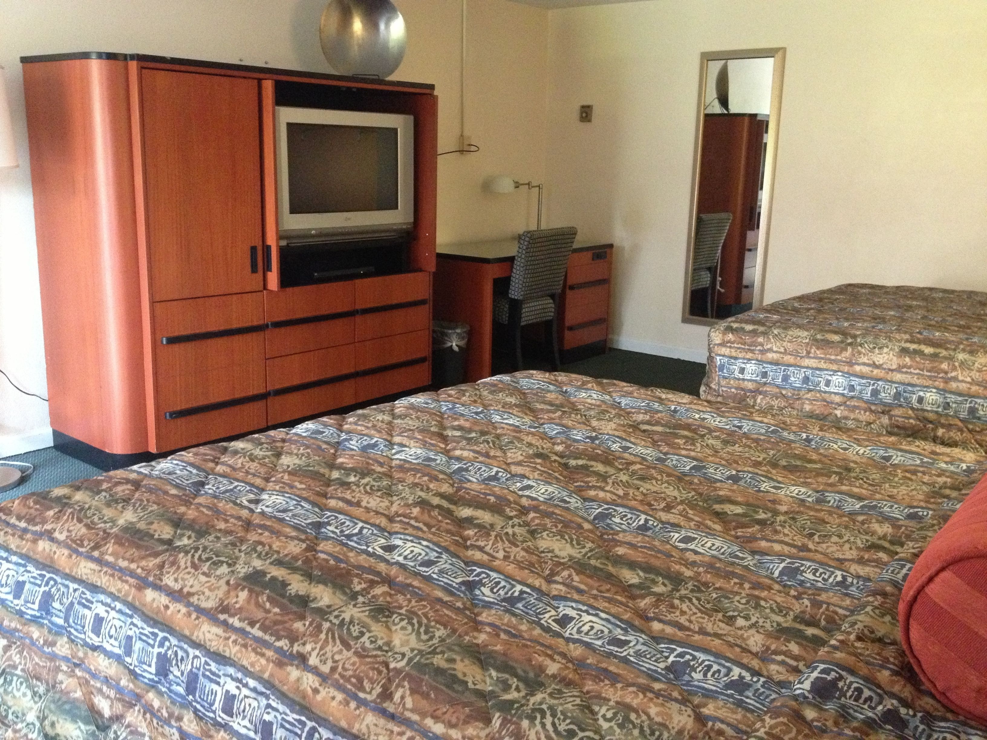 A room with a bed, a dresser, a television, a desk, and a mirror.