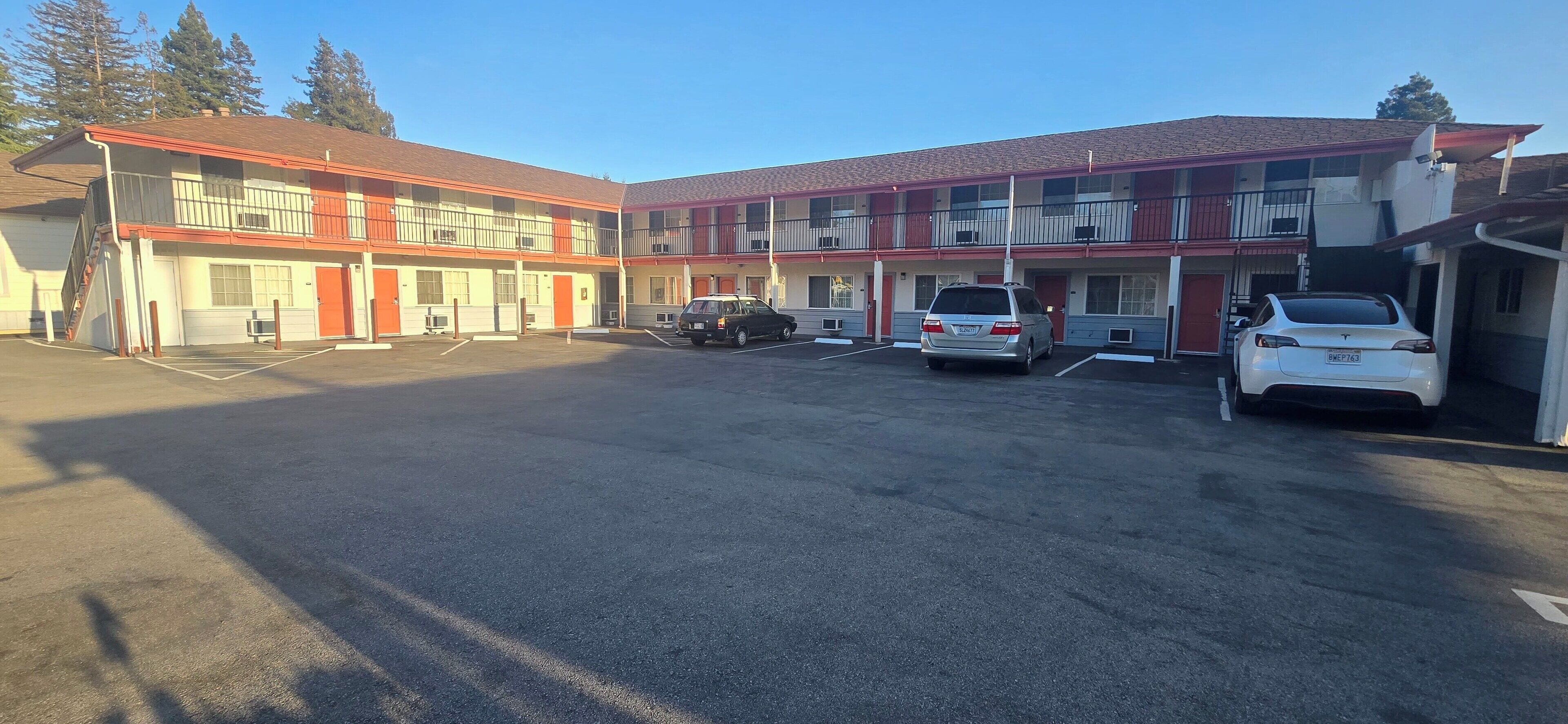 A motel with two-story buildings, a parking lot, and several cars parked in front.