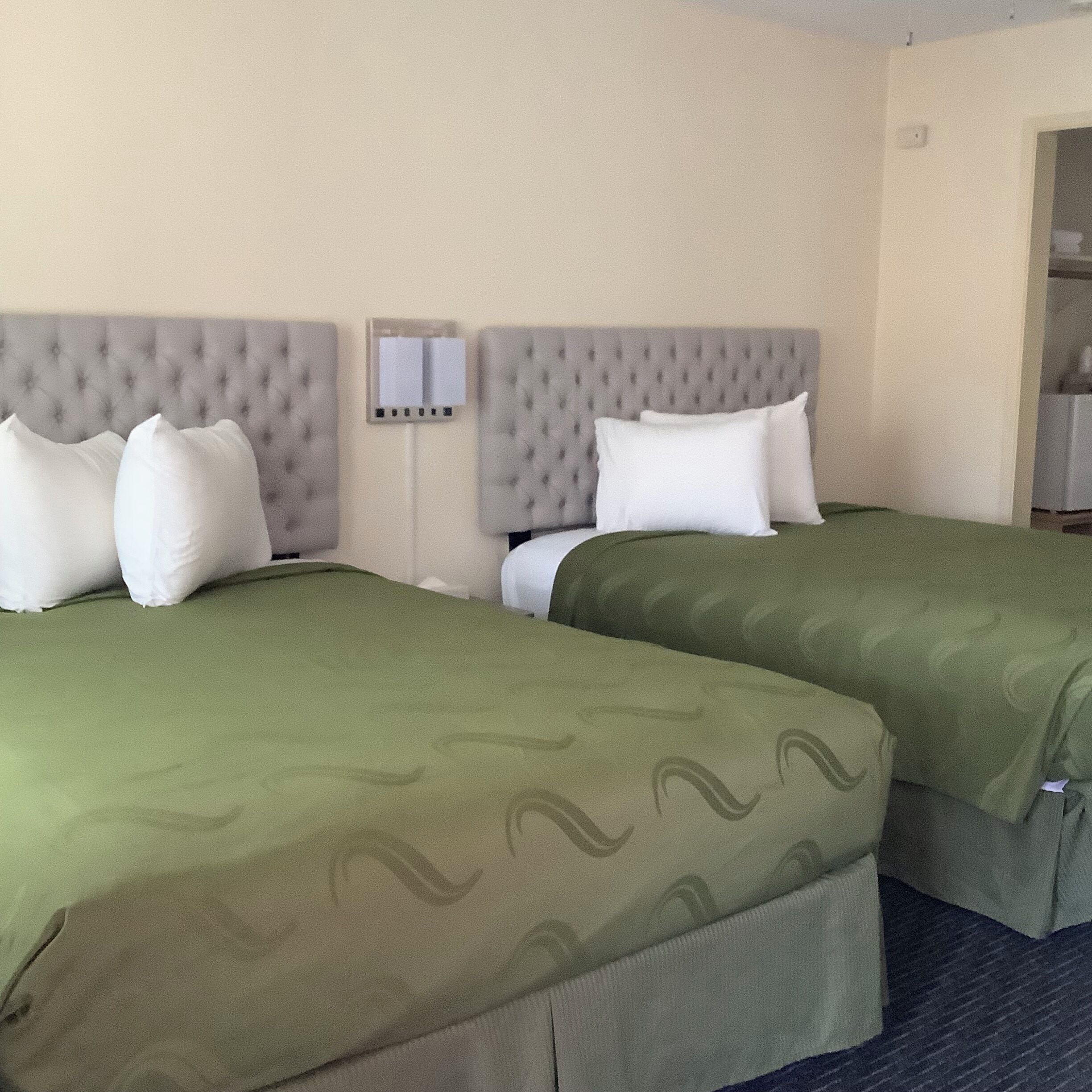 A hotel room with two beds, each with a green bedspread and white pillows.