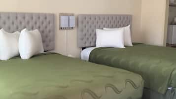 A hotel room with two beds, each with a green bedspread and white pillows.