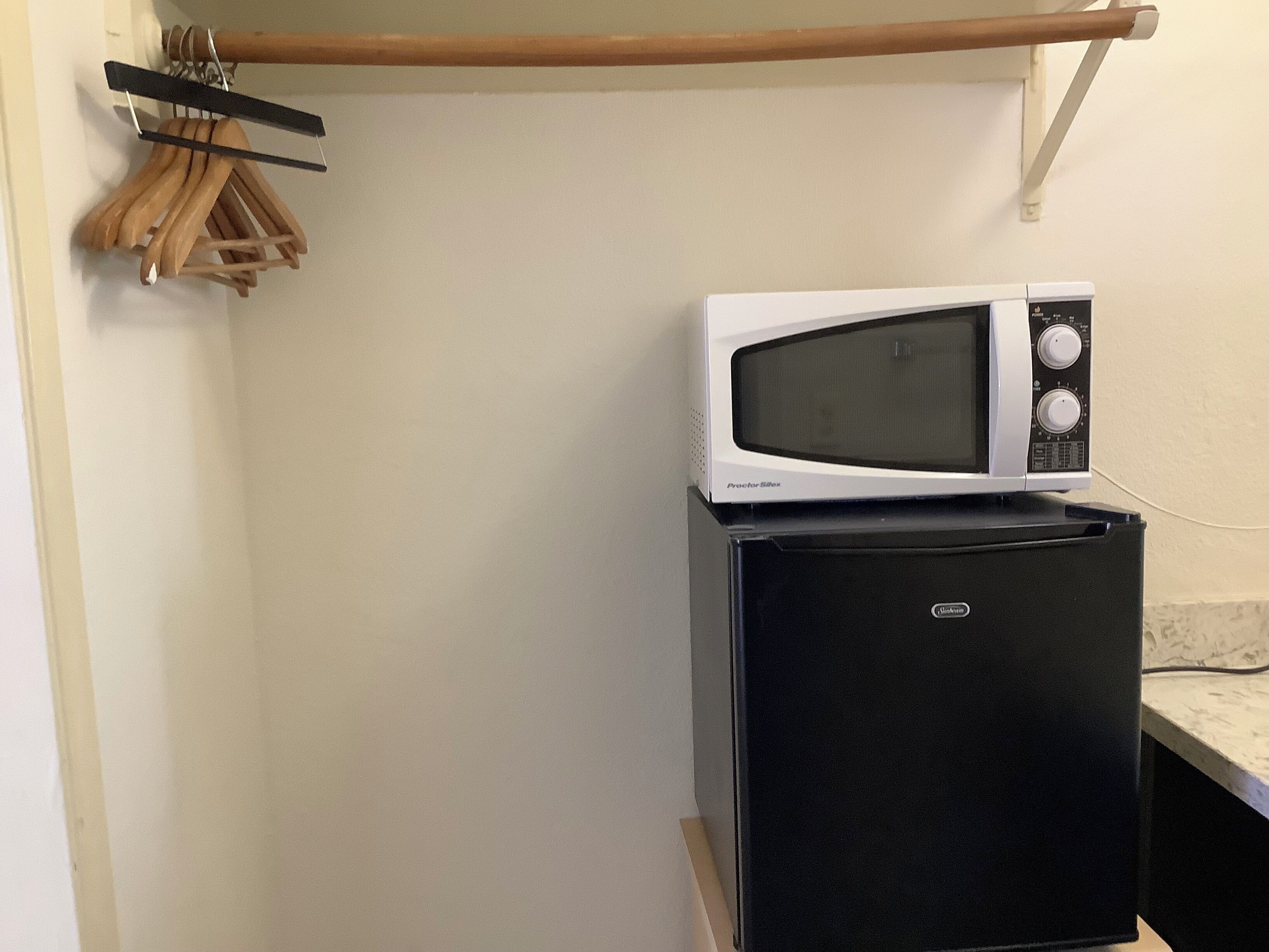 Cozinha compacta com micro-ondas branco sobre geladeira preta, cabides de madeira em um suporte e uma viga de madeira acima.