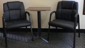 Two black chairs and a small table in a room with a carpeted floor and plain walls. - National 9 Santa Cruz (Santa Cruz)