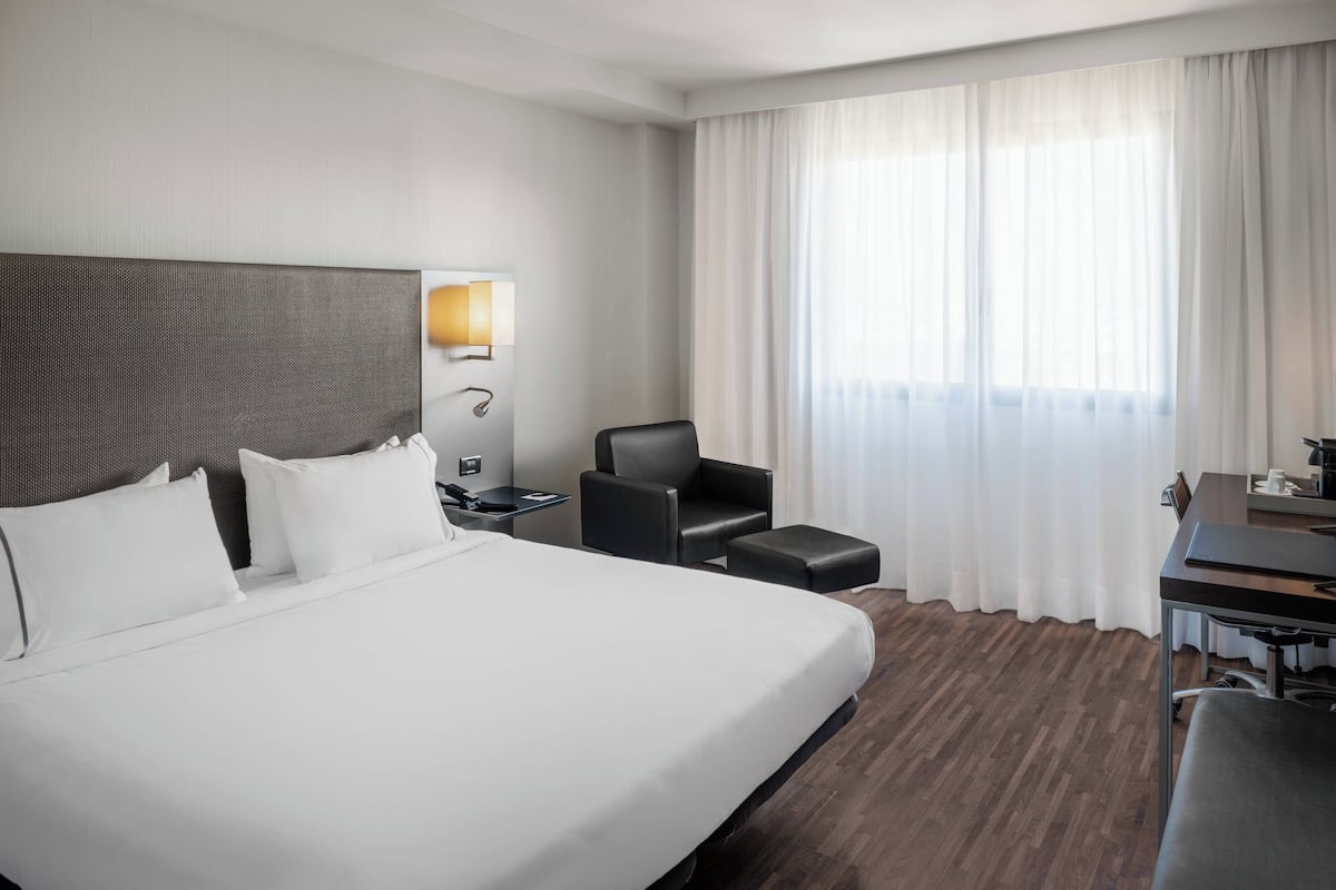 A hotel room with a large bed, a desk, a chair, and a lamp.