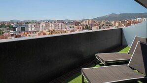 Uma varanda com duas poltronas de descanso, vista para a paisagem urbana e uma montanha ao longe.