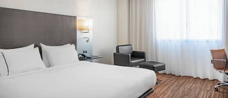 A hotel room with a large bed, a desk, a chair, and a window with curtains.