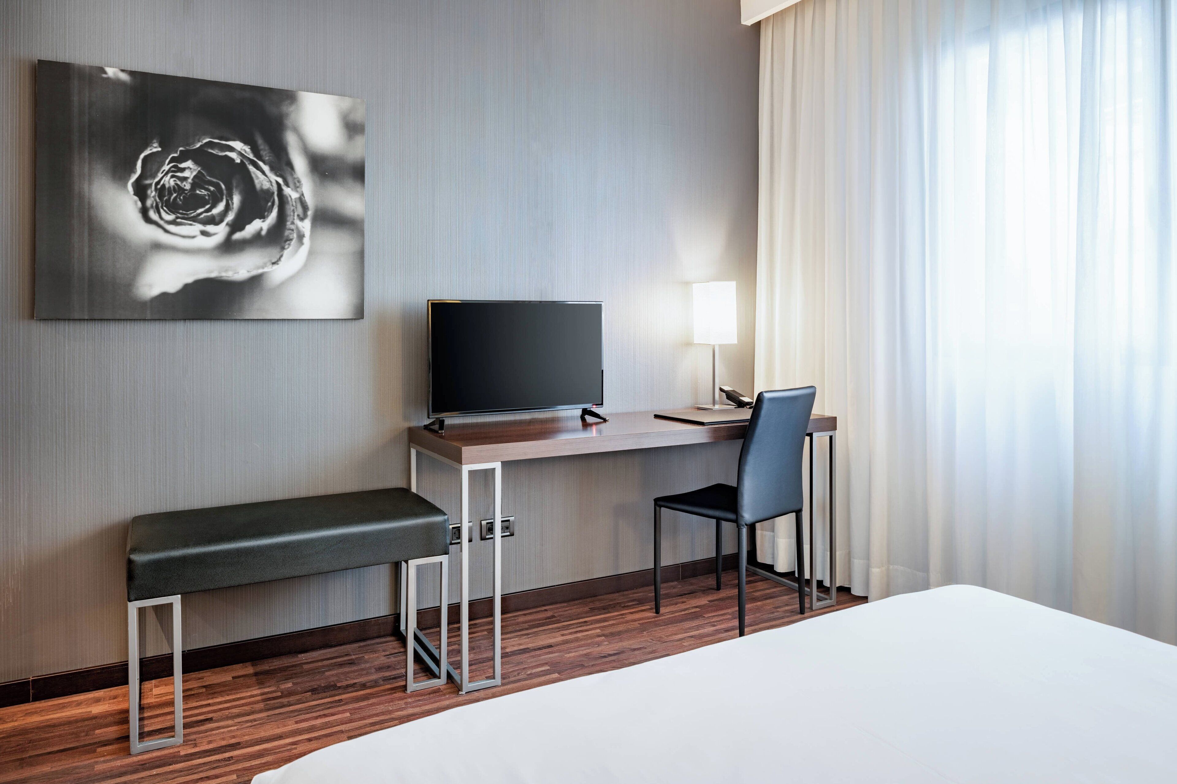 Hotelkamer met een bed, bureau met een flatscreen televisie, stoel, bankje en een groot abstract schilderij aan de muur.