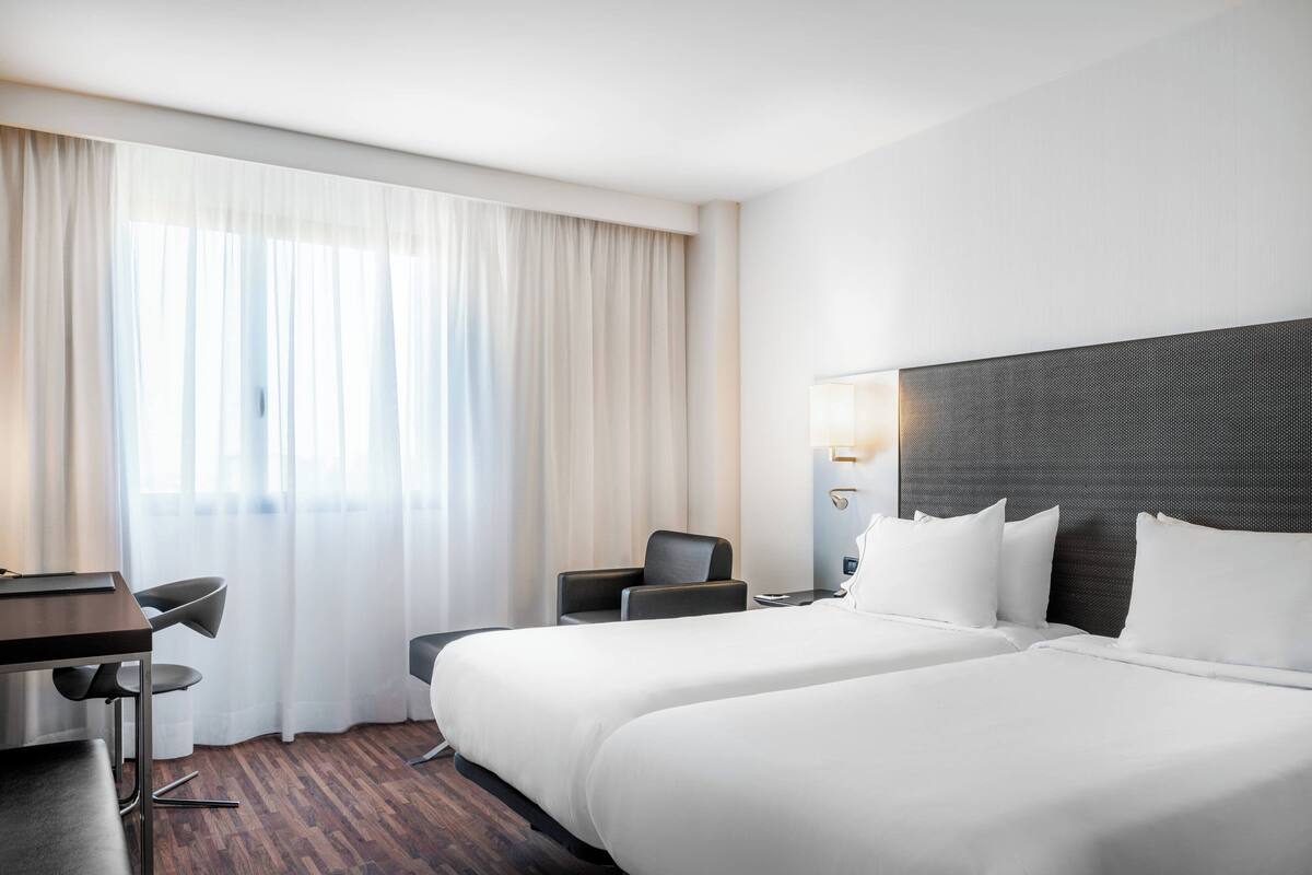 A hotel room with a large bed, a desk with a chair, and a window with curtains.