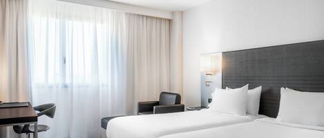 Une chambre d’hôtel avec un grand lit, un bureau avec une chaise et une fenêtre avec des rideaux.