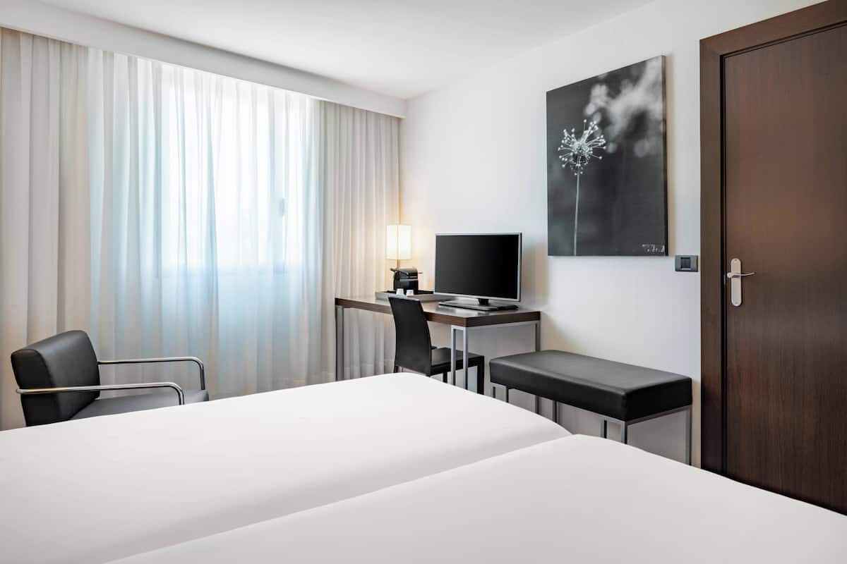 A hotel room with a bed, a desk with a computer, a chair, and a TV.