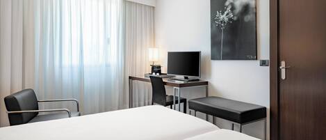 A hotel room with a bed, a desk with a computer, a chair, and a TV.