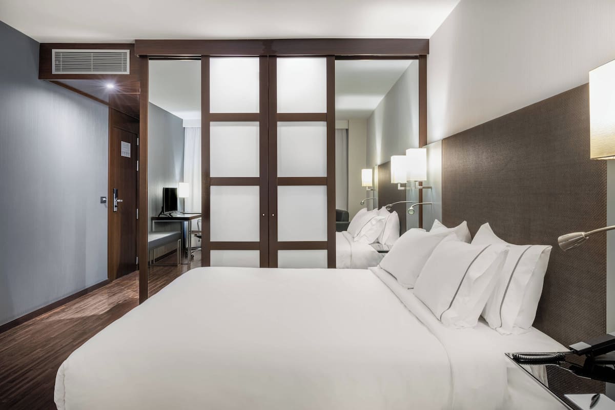 A hotel room with a large bed, a desk, and a wardrobe with sliding doors.