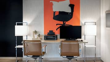 Un espacio de oficina moderno con dos escritorios, sillas, un monitor grande, una impresora y un elemento decorativo en la pared.