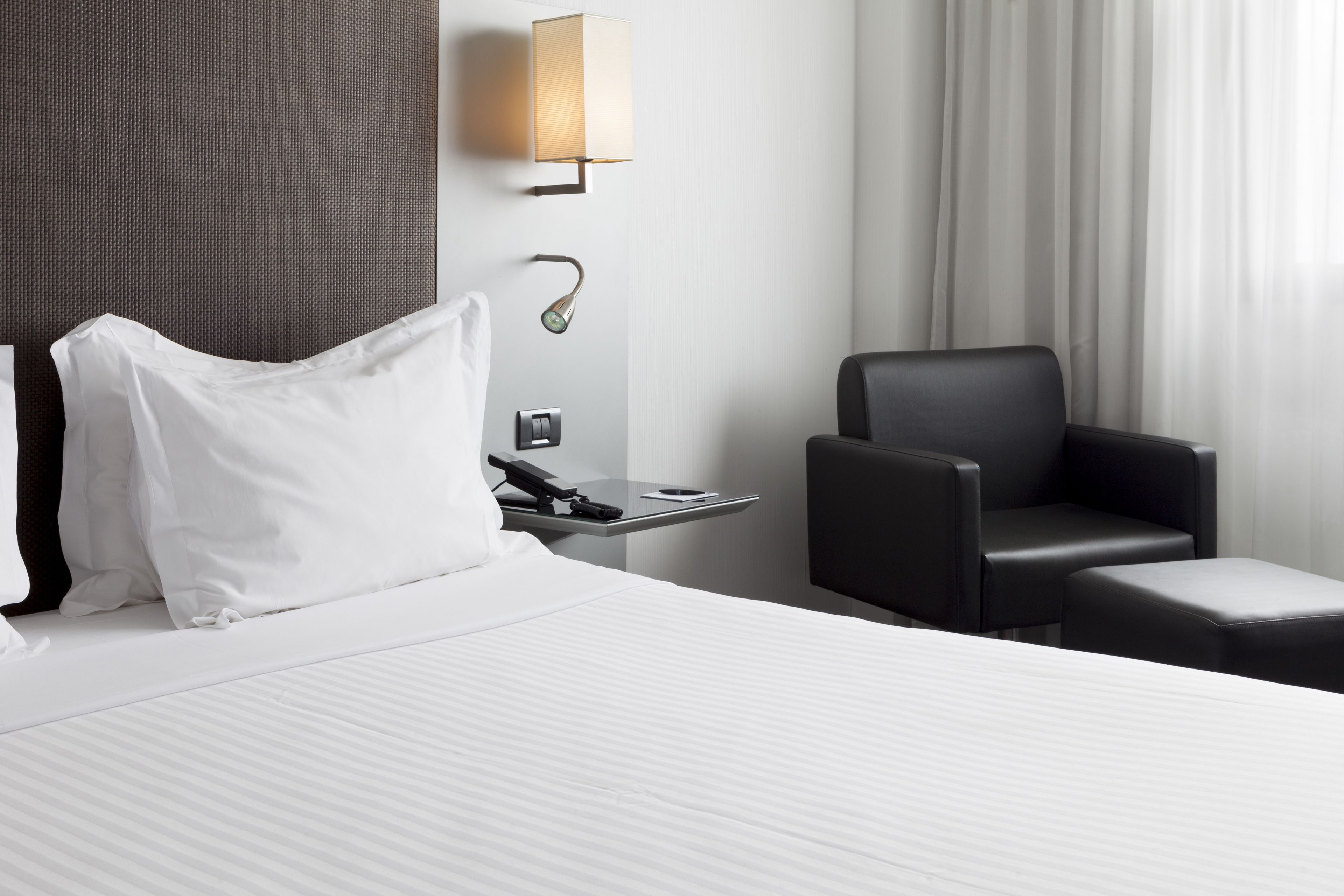 Habitación de hotel con cama, escritorio con lámpara, una silla y ventana con cortinas.