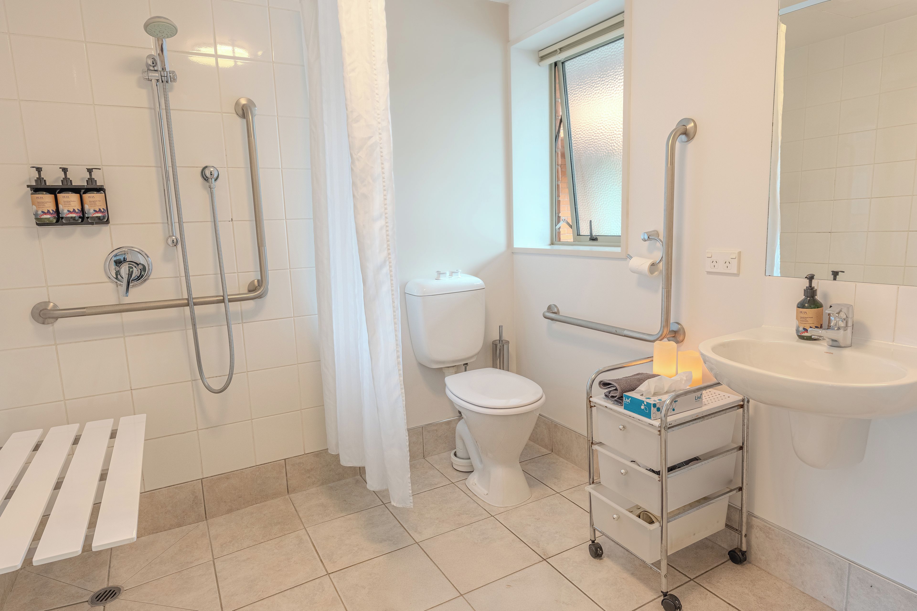 A bathroom with a shower, toilet, sink, and a handrail.