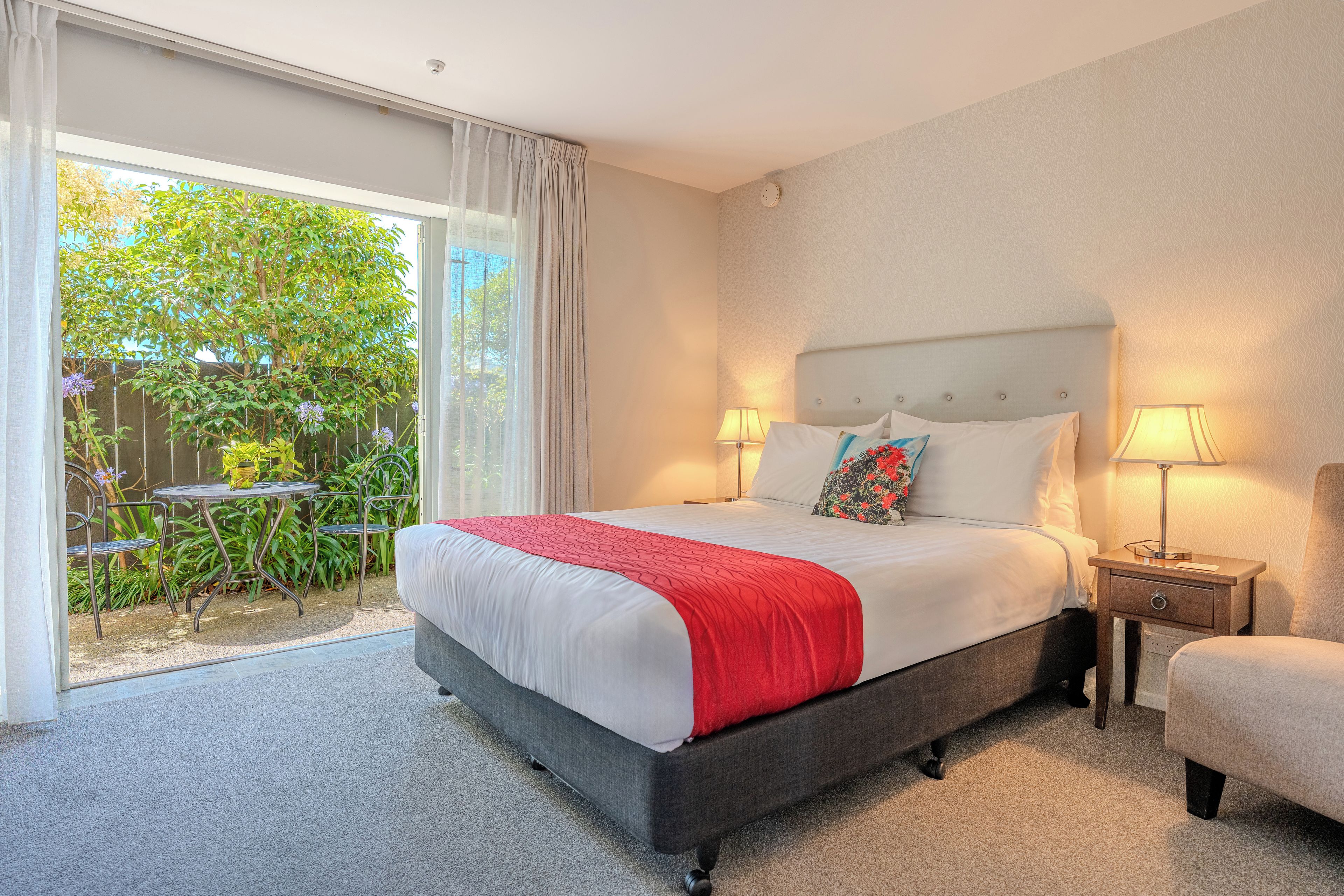 A hotel room with a bed, two bedside lamps, a small table, and a chair.