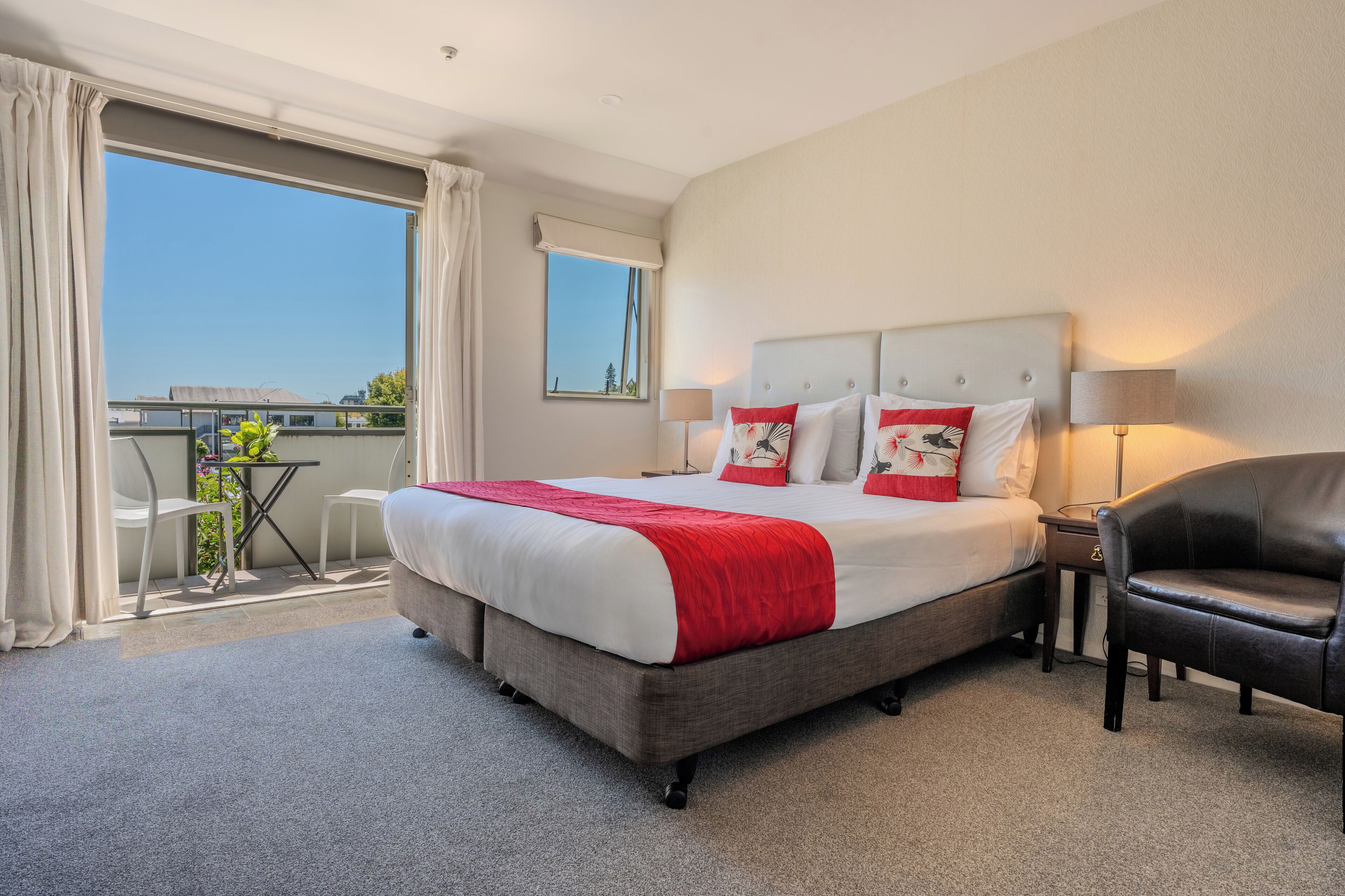 A hotel room with a large bed, a chair, a table, and a balcony with a view.