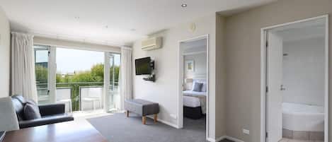A modern hotel room with a balcony, a flat-screen TV, a bed, a bathroom with a bathtub, and a wooden table.