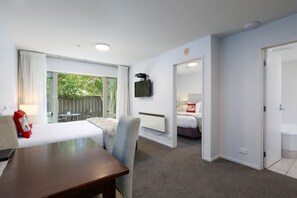 A hotel room with a bed, a desk, a chair, a TV mounted on the wall, and a view of the outdoors. - Chelsea Park Motor Lodge Nelson (Nelson)
